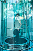 Frau steht und schaut aus einem runden Glasaufzug; Lugano, Tessin, Schweiz