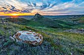 Man stands on mound in the vast landscape stretching to the horizon at sunset in Grasslands National Park; Val Marie, Saskatchewan, Canada