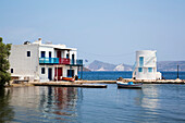 Dorf Embourios mit einem Wohnhaus am Wasser und einem kleinen Boot am Kai; Embourios, Insel Milos, Kykladen, Griechenland.