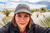 Young woman taking a self-portrait with desert plants and white sand in the background, White Sands National Monument; Alamogordo, New Mexico, United States of America