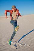 A young woman leaps in the air on the white sand with blue sky, White Sands National Monument; Alamogordo, New Mexico, United States of America
