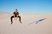 Unbekümmerter Mann in der Luft auf weißem Sand mit blauem Himmel, der einen Schatten neben ihn wirft, White Sands National Monument; Alamogordo, New Mexico, Vereinigte Staaten von Amerika.