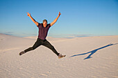 Carefree man in mid-air on the white sand with blue sky, casting a shadow beside him, White Sands National Monument; Alamogordo, New Mexico, United States of America