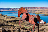 Metal art depicting wild horses running across a ridge atop the Wild Horse Monument near the town of Vantage in Eastern Washington. Wanapum Lake formed by a dam on the Columbia River and the I-90 Bridge in the background; Vantage, Washington, United States of America