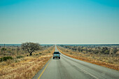 Ein Lastwagen fährt auf einer offenen Straße in der Wüste mit einem großen blauen Himmel am Horizont; Namibai.