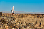 Female tourist stands looking out over Fish River Canyon; Namibia