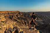 Männlicher Tourist steht auf einem Felsvorsprung mit Blick auf den Fischfluss-Canyon; Namibia.