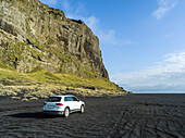 Car on a black landscape with rocky outcrop in Southern Iceland; Myrdalshreppur, Southern Region, Iceland