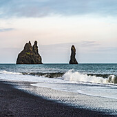 Rock formations along the coastline of the Southern Region of Iceland, with the surf washing up onto black sand in the foreground; Myrdalshreppur, Southern Region, Iceland
