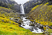 Ein Wasserfall über einer felsigen Landschaft mit einem über die Felsen stürzenden Fluss; Djupivogur, Ostregion, Island.