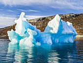 Eisberg im blauen Wasser vor der zerklüfteten Küste Grönlands; Sermersooq, Grönland