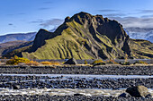Rugged land formation covered in green foliage with water flowing in the foreground; Rangarthing eystra, Southern Region, Iceland