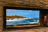 View Of Dunstanburgh Castle from a pier with a cement structure on Craster Harbour; Craster, Northumberland, England