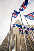 Wide angle of a grey concrete church, Hallgrimskirkja, and Icelandic flags; Reykjavik, Reykjavik, Iceland