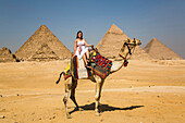 Weibliche Touristin auf einem Kamel, Pyramidenkomplex von Gizeh, UNESCO-Weltkulturerbe; Gizeh, Ägypten.