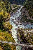 Aerial view of an abandoned suspension bridge along the Gokyo and Everest Base Camp treks, decorated with prayer flags over the rushing Dudh Kosi River and surrounding cliffs and forest; Solokhumbu District, Nepal