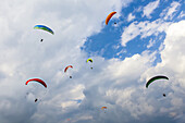 A group of colorful paragliders playing in the thermals above Sarangkot and the city of Pokhara on a sunny autumn day with a cloudy sky; ?Kaski District, Nepal