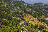 A colourful paraglider playing in the thermals above the terraces of Sarangkot, Pokhara, Nepal on a sunny and cloudy autumn day; Pokhara, Nepal