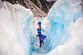 Reisende betreten einen Eistunnel bei der Erkundung des berühmten Franz-Josef-Gletschers mit seinen blauen Eishöhlen, tiefen Gletscherspalten und Tunneln, die die ständig wechselnden Eisformationen markieren; Westküste, Neuseeland