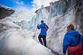 Reisende erkunden den berühmten Franz Josef Gletscher mit seinen blauen Eishöhlen, tiefen Gletscherspalten und Tunneln, die die sich ständig verändernden Eisformationen kennzeichnen; Westküste, Neuseeland