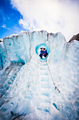 Reisende erkunden Neuseelands berühmten Franz-Josef-Gletscher. Blaues Eis, tiefe Gletscherspalten, Höhlen und Tunnel kennzeichnen das sich ständig verändernde Eis; Westküste, Neuseeland