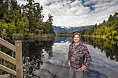 Porträt eines Reisenden, der den Lake Matheson an einem bewölkten Tag erkundet, der die berühmten Spiegelungen des Mount Cook und des Mount Tasman etwas abschwächt; South Westland, Neuseeland