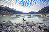 Man cautiously walking out into the water of the icy glacial lakes of Mount Cook National Park; Canterbury, New Zealand