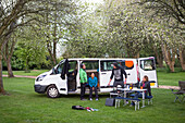 Friends setting up camp outside of a modified caravan camper; Bourton-on-the-Water, England, United Kingdom