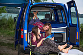 Campsite set up along Lake Balton for the day with travelers hanging out in camper van looking at magazine; Zamardi, Somogy County, Hungary