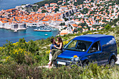 Travellers explore the surrounding cliffs above Dubrovnik with their vehicle to catch the stunning views over the coastal city. A young couple has an intimate moment beside their camper van; Dubrovnik, Dubrovacko-neretvanska zupanija, Croatia