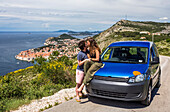 Travelers explore the surrounding cliffs above Dubrovnik with their car to catch the stunning views over the coastal city. A young couple kisses by their camper van; Dubrovnik, Dubrovacko-neretvanska zupanija, Croatia