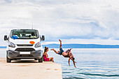 Eine Gruppe von Reisenden hält für ein frühmorgendliches Bad im Meer an, nachdem sie auf einem Road Trip in ihrem Van gezeltet haben; Podgora, Gespanschaft Split-Dalmatien (Splitsko-dalmatinska zupanija), Kroatien