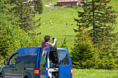 Ein Tourist macht eine Pause am Fuße der Alpen, bevor er über Österreichs höchsten Gebirgspass fährt, und fotografiert landwirtschaftliche Flächen am Hang auf der Großglockner Hochalpenstraße; Österreich
