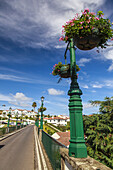 Lampposts filled with flowering planters line the road and historical bridge in the picturesque town of Nordeste; Sao Miguel Island, Azores