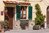 Traditionelles Stuckhaus mit hölzerner Eingangstür und Fenster mit grünen Fensterläden an einem sonnigen Tag in der Stadt Cortona; Arezzo, Toskana, Italien