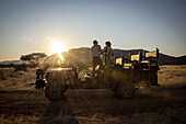 Safari guide speaking with guests while standing in a jeep on the savanna at the Gabus Game Ranch at sunrise; Otavi, Otjozondjupa, Namibia