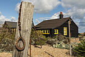 Prospect Cottage, ehemals im Besitz des verstorbenen Künstlers und Filmregisseurs Derek Jarman, mit seinem Garten am Meer und den eingemeißelten Buchstaben des John Donne-Gedichts 'The Sun Rising' an der Außenwand des Cottages; Dungeness, Kent, England, Vereinigtes Königreich.