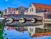 Medieval arch bridge crossing a canal with old stone buildings reflected in the water; Vrboska, Hvar Island, Croatia