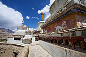Nahaufnahme eines Betonwegs durch die weiß getünchten buddhistischen Stupas (in der tibetischen Kultur als Chortens bekannt) und Gebetsmühlen im Kloster Lamayuru oberhalb des Industals, in den Himalaya-Bergen von Ladakh, Jammu und Kaschmir; Lamayuru, Ladakh, Indien.