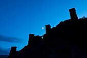 Dämmerung über den mittelalterlichen Festungstürmen von Keselo, die die Silhouette des Berghangs vor dem Hintergrund des Mondes im Tuscheti-Nationalpark zeichnen; Omalo, Kachetien, Georgien.