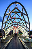 Die bogenförmige Fußgängerbrücke des Friedens, beleuchtet in der Abenddämmerung, überspannt den Fluss Mtkvari (Kura) und verbindet den Rike Park mit der Altstadt von Tiflis; Tiflis, Georgien.