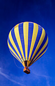 Yellow and blue striped hot air balloon in mid-flight against a blue sky; Phoenix, Arizona, Untied States of America