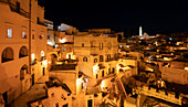 Nachtpanorama der antiken Höhlenwohnungen mit dem Glockenturm des Doms von Matera über der Stadt; Matera, Basilikata, Italien
