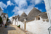 Straßenszene mit einer Reihe traditioneller apulischer Trulli-Häuser aus rundem Stein in der Stadt Alberobello; Alberobello, Apulien, Italien.