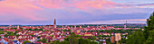 Blick über die Stadt Regensburg vom Dreifaltigkeitsberg mit den Türmen des gotischen Doms St. Peter am Horizont bei Sonnenuntergang mit rosa Wolken; Regensburg, Bayern, Deutschland