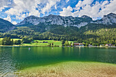Reflection of the grassy shore surrounding Lake Hintersee below the Bavarian Alps with lodgings and people enjoying the water in pedal boats; Berchtesgadener Land, Ramsau, Bavaria, Germany