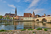 Outlook over the Danube River with the old, 12th Century Stone Bridge and the Gothic St Peter's Cathedral from the stone path at Marc?-Aurel-shore in the Old Town of Regensburg with a blue sky at sunset; Regensburg, Bavaria, Germany