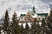 Prince Of Wales Hotel im Winter, eingerahmt von immergrünen Bäumen und schneebedeckten Bergen; Waterton Alberta Kanada