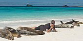 Ein Mann liegt auf einem weißen Sandstrand mit den Seelöwen (Otariidae); Galapagos Equador