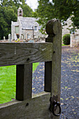 Ein offenes Tor, das einen Weg zu einem Friedhof und einer Kirche hinunterführt; Northumberland England